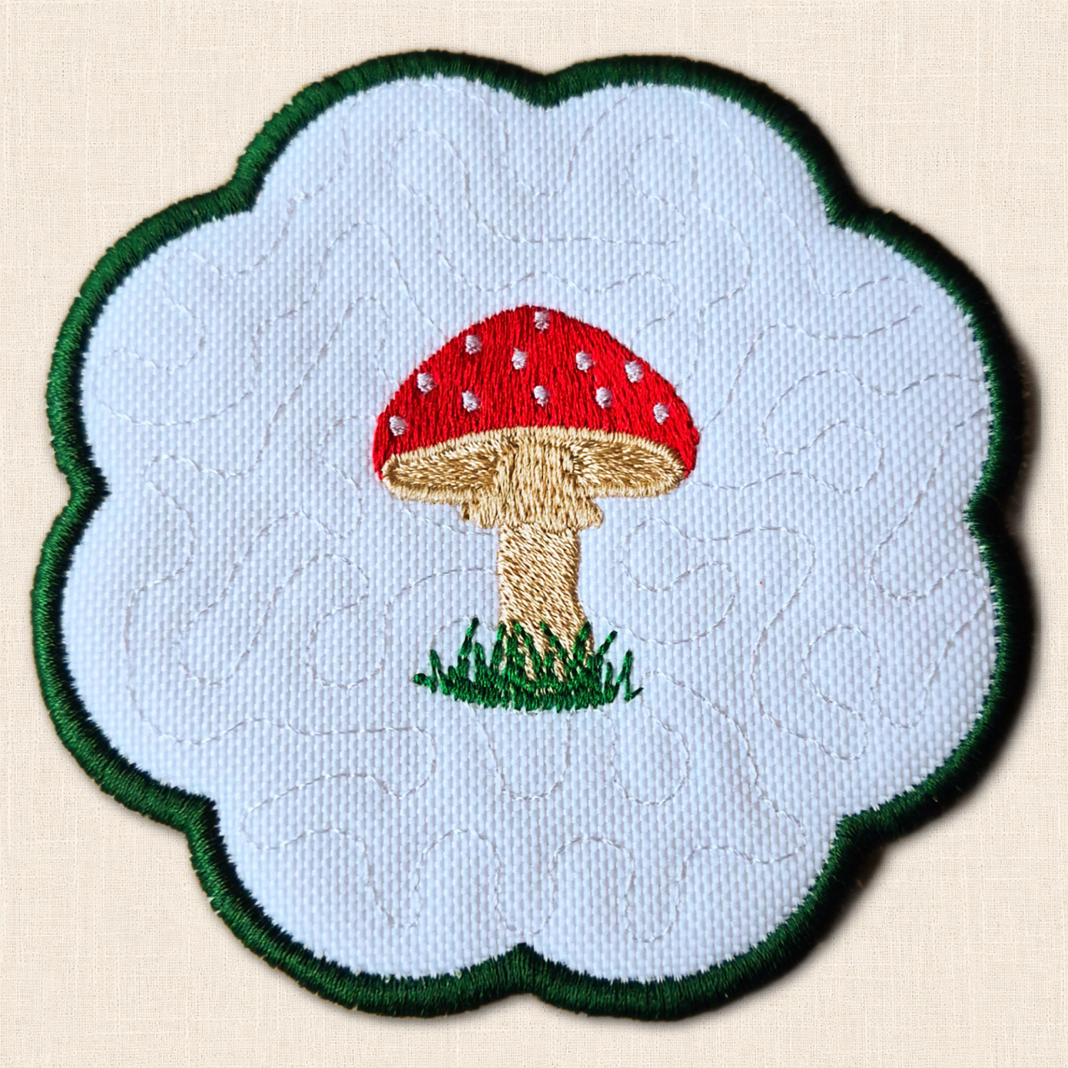 Close-up of Toadstool Candle Coaster showing red and white embroidered mushroom, beige stem and green stitched border