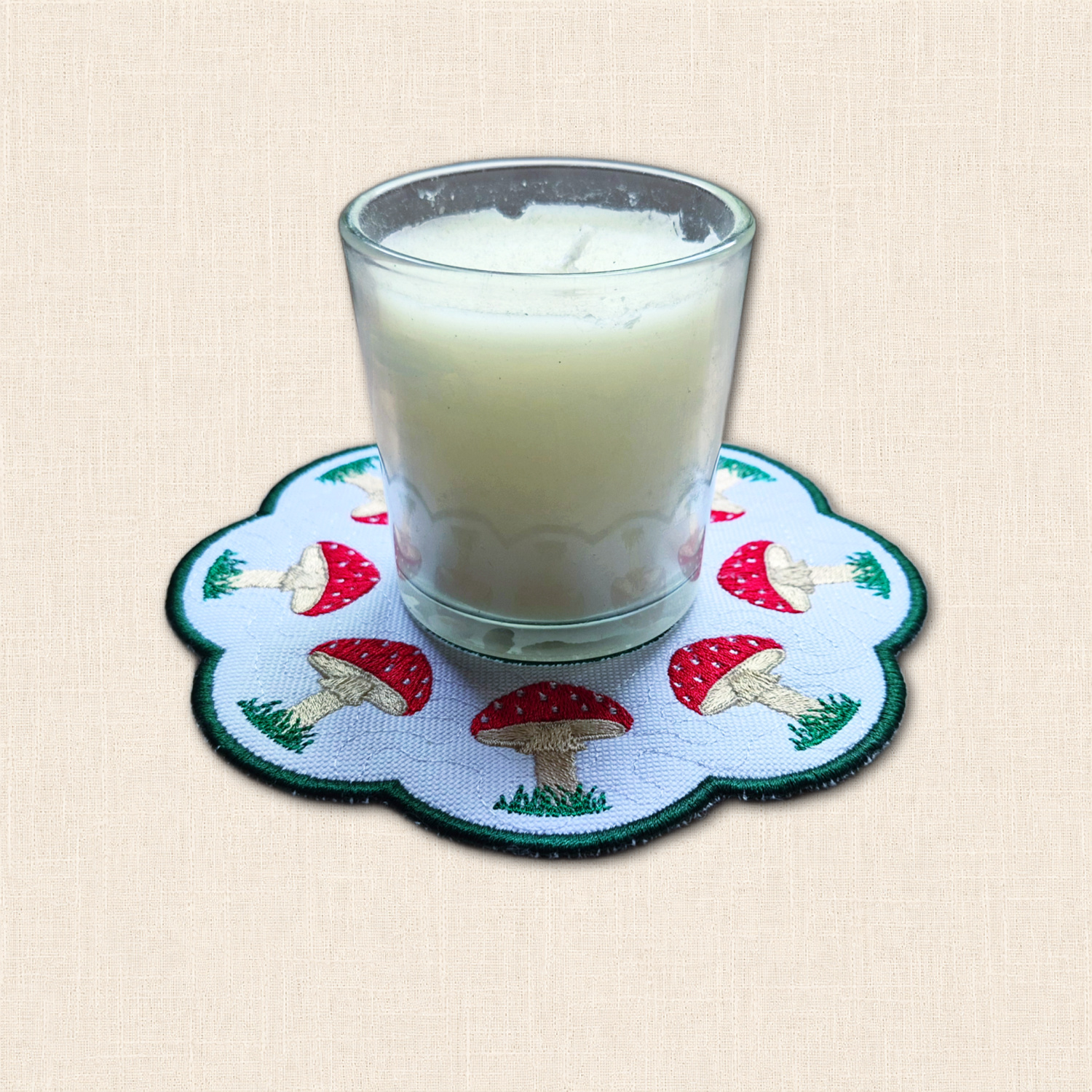 Embroidered Toadstool Candle Mat with glass candle jar, red and white mushrooms, grassy details and scalloped edge