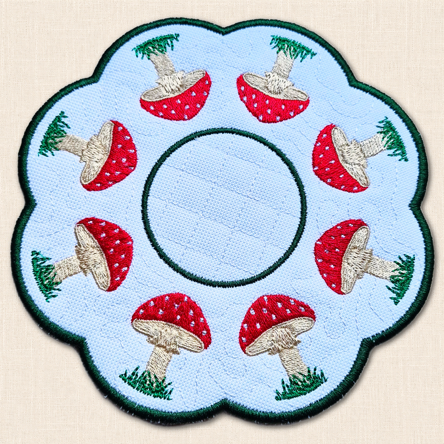 Toadstool Candle Mat viewed from above with embroidered red and white mushrooms, grassy details and circular centre