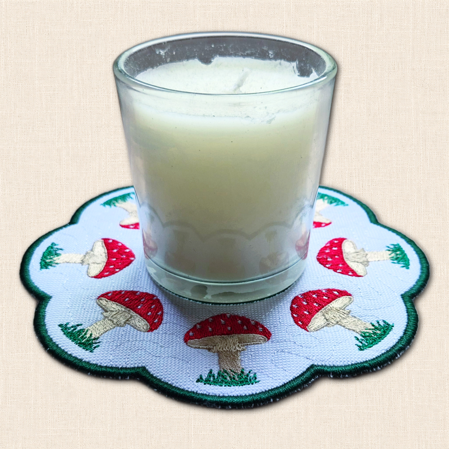 Close-up of embroidered Toadstool Candle Mat with candle jar, red spotted mushrooms and green stitched border