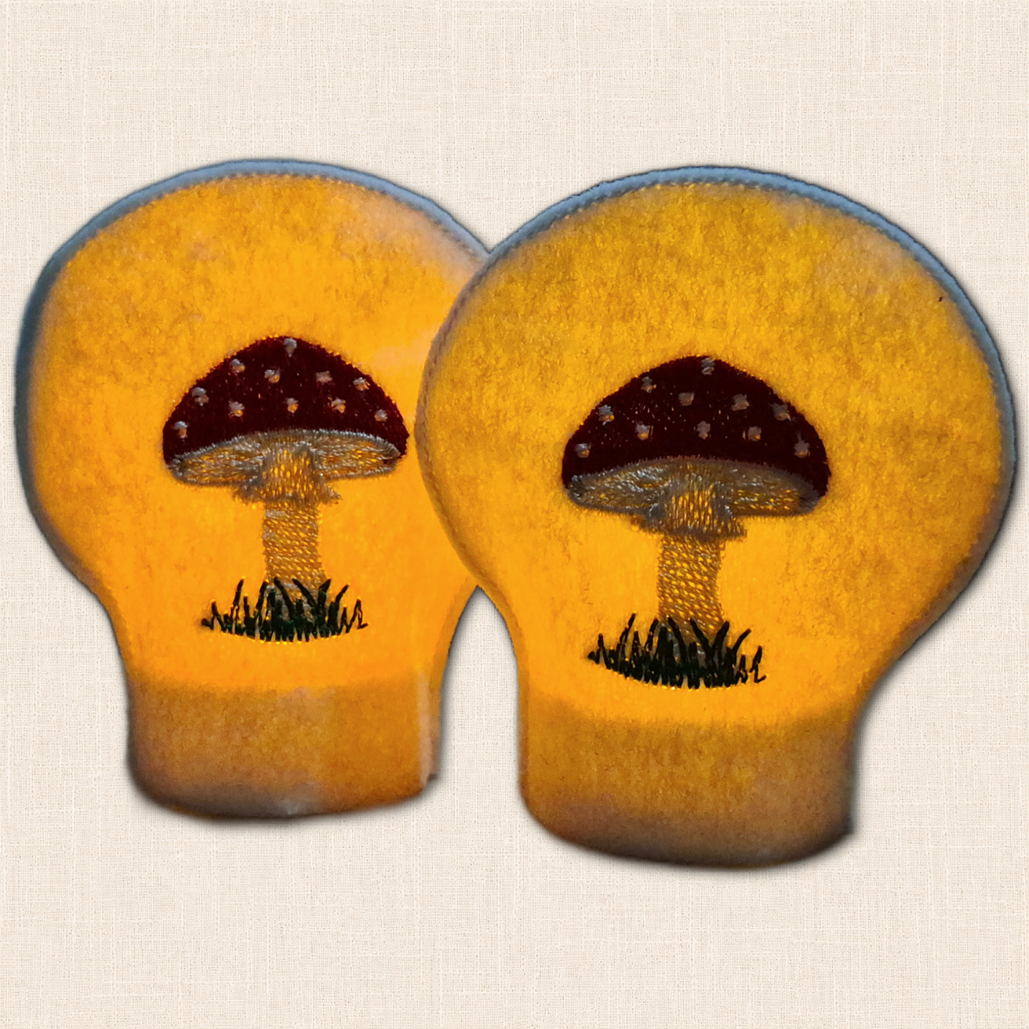 Pair of Toadstool felt tealight covers glowing over LED tealights with embroidered red and white mushrooms