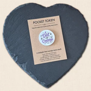 A Dot of Courage pocket token on kraft backing card with purple wording, displayed on a slate heart photography prop.