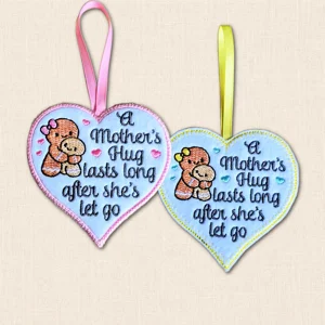 Two white felt 'A Mother's Hug' hearts with gingerbread mum and child embroidery, showing pink satin stitch and yellow blanket stitch borders.