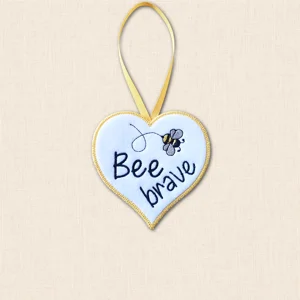 Bee Brave felt heart hanger with black embroidered wording, a grey and golden yellow bee, looping flight trail and yellow ribbon.