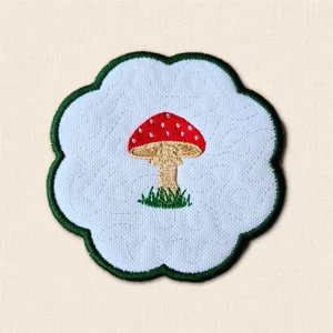 Embroidered Toadstool Candle Coaster with red spotted mushroom, grassy detail, stitched background and green scalloped edge