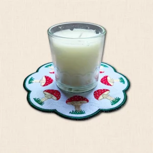 Embroidered Toadstool Candle Mat with glass candle jar, red and white mushrooms, grassy details and scalloped edge