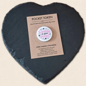 Friendship in Your Pocket pocket token with pink wording and black heart details on a kraft backing card, displayed on a slate heart photography prop.