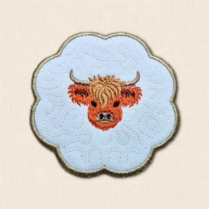 Highland Cow embroidered candle coaster with scalloped edge, stitched background pattern and central cow face