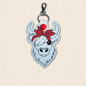 Embroidered Highland cow keyring with long horns, shaggy stitched detail and a colourful bandana bow.