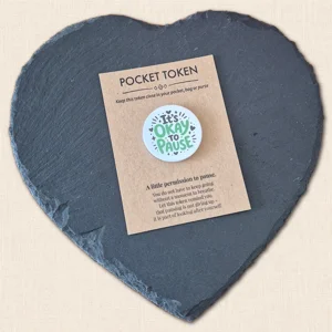It's Okay to Pause pocket token with green highlighted wording and black heart and star details on a kraft backing card, displayed on a slate heart photography prop.