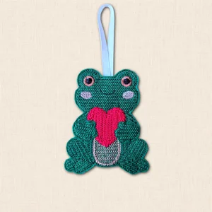 Green embroidered Knit Stitch Frog Heart Hanging Decoration holding a bright pink heart against its belly, finished with a pale ribbon loop.