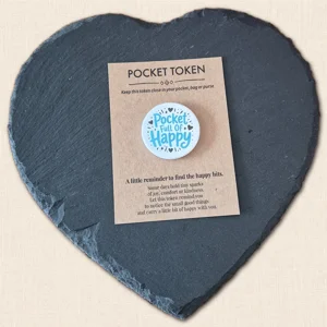 Pocket Full of Happy pocket token with blue wording and black heart and star details on a kraft backing card, displayed on a slate heart photography prop.