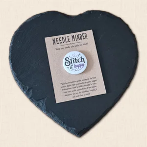 Stitch It Happy magnetic needle minder on a kraft presentation card displayed on a black heart-shaped slate