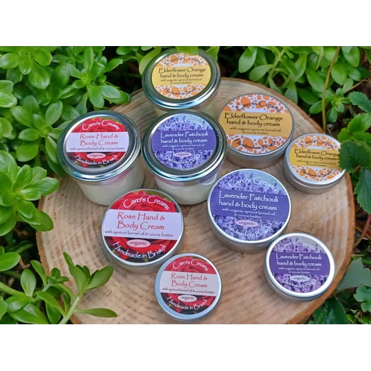 A collection of 3 sizes of round pots containing handmade organic natural hand and body cream in various sizes. The labels feature floral designs and text including Rose, Lavender Patchouli, and Elderflower Orange, with the brand name Caro's Creams visible.