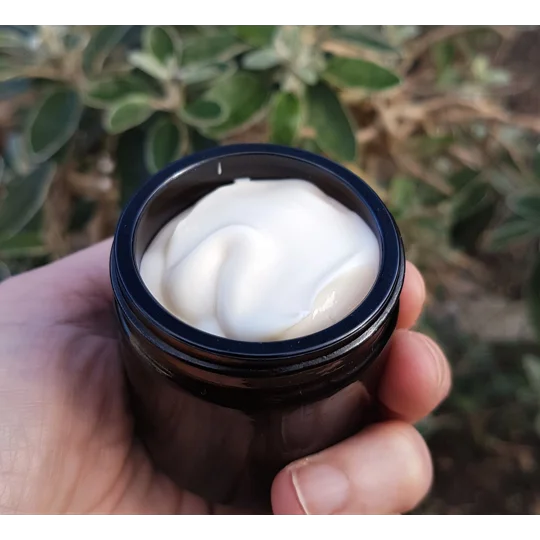 a small, cylindrical, dark brown glass jar filled with a thick, smooth cream. The jar has a simple, circular opening and a dark rim, showcasing the opaque, off-white texture of the contents within the container.