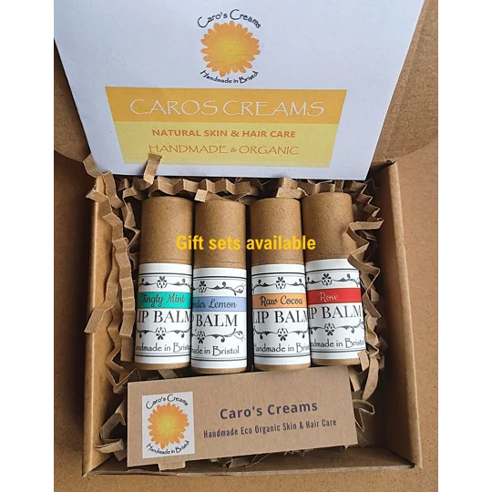 Text reads "Gift Sets Available". A gift set of four biodegradable lip balm tubes in a brown cardboard box with crinkle paper. The tubes feature labels with the text Caro's Creams, Raw Cocoa, Tingly Mint, Rose, and Lavender Lemon. A circular Caro's Creams logo with a yellow and orange calendula flower, and Handmade in Bristol is visible on a small kraft card.