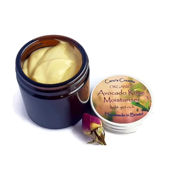 May include: A brown glass jar with a white lid containing a yellow cream. The lid has a label that reads "Caro's Creams Organic Avocado Rose Moisturiser light yet rich Handmade in Bristol."
