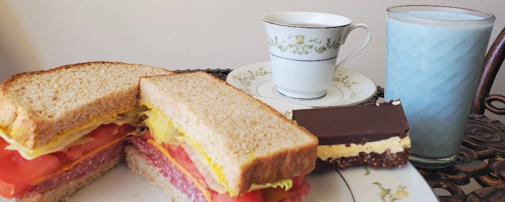 a delisous light lunch feturing a ham sandwich, a cup of tea a Nanaimo bar and a blue pea flower matcha.