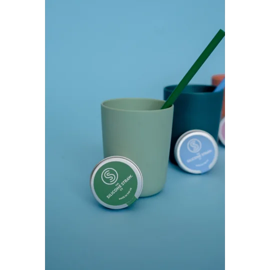 A silicone straw in a small cup with a carry tin next to it