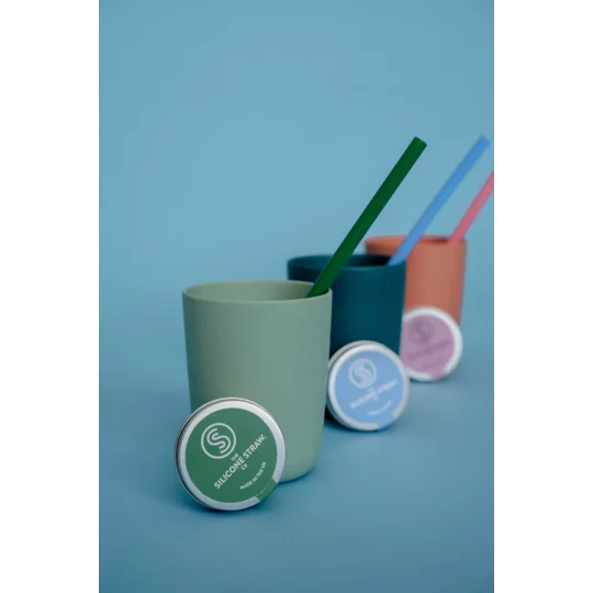 Reusable silicone straws in a cup beside a reusable straw travel case. Three in a line