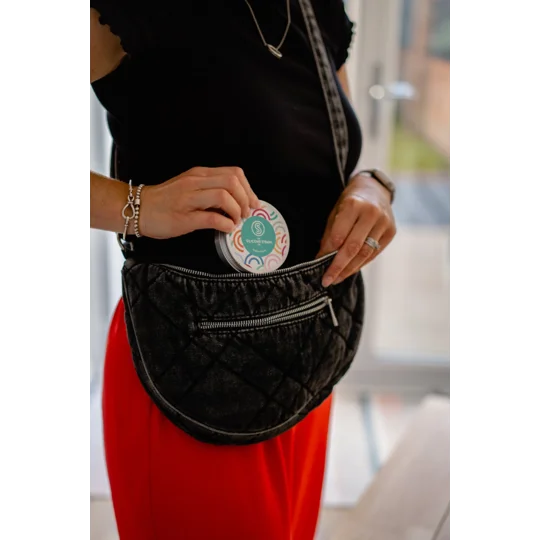 A person putting a reusable straw in a travel tin in a handbag