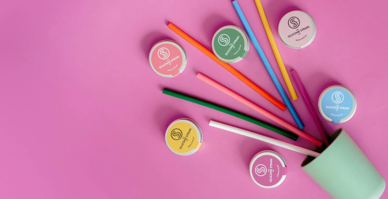 Colourful silicone straws and travel tins spilling from a cup
