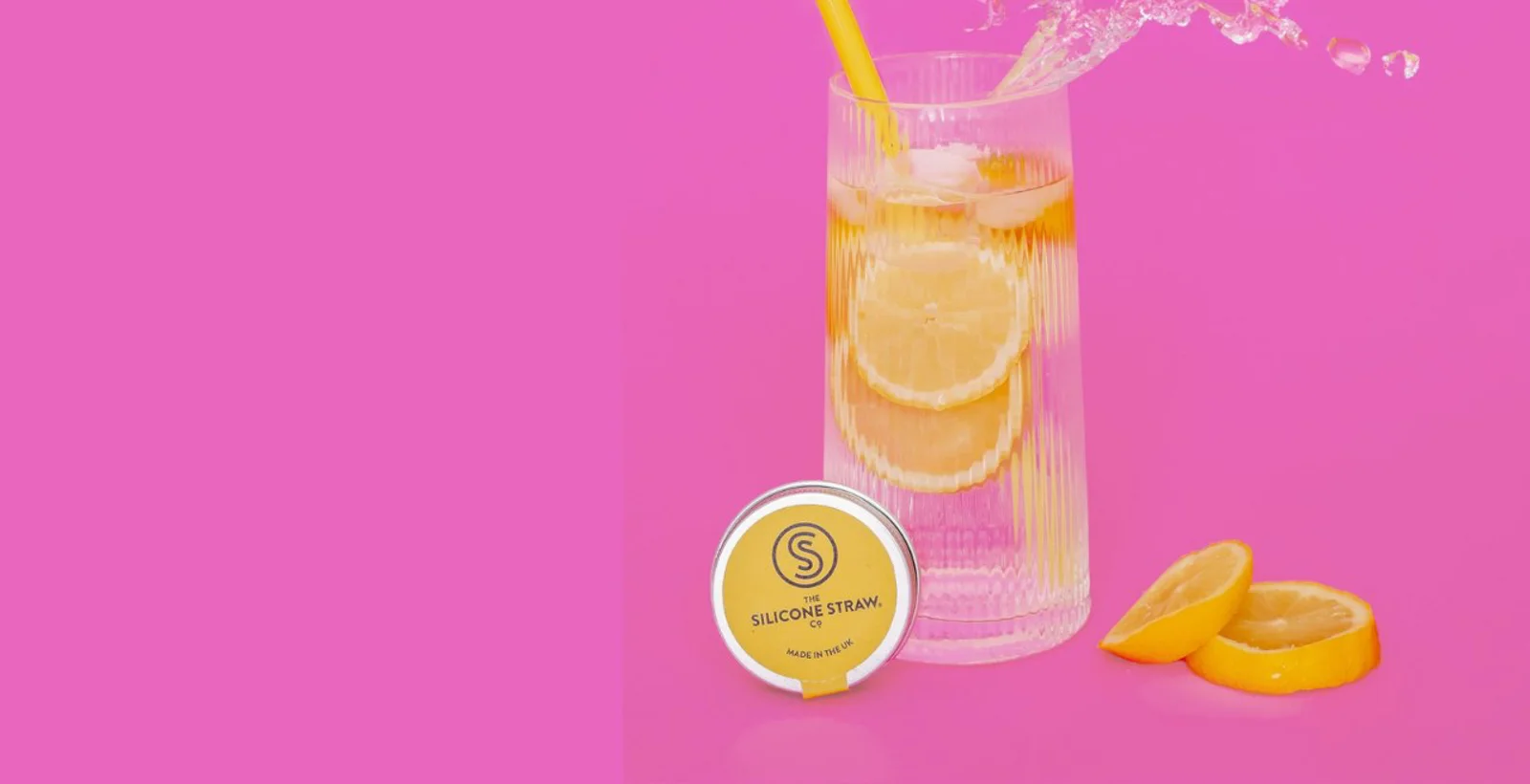 A glass of iced lemonade with a yellow silicone straw beside its travel tin