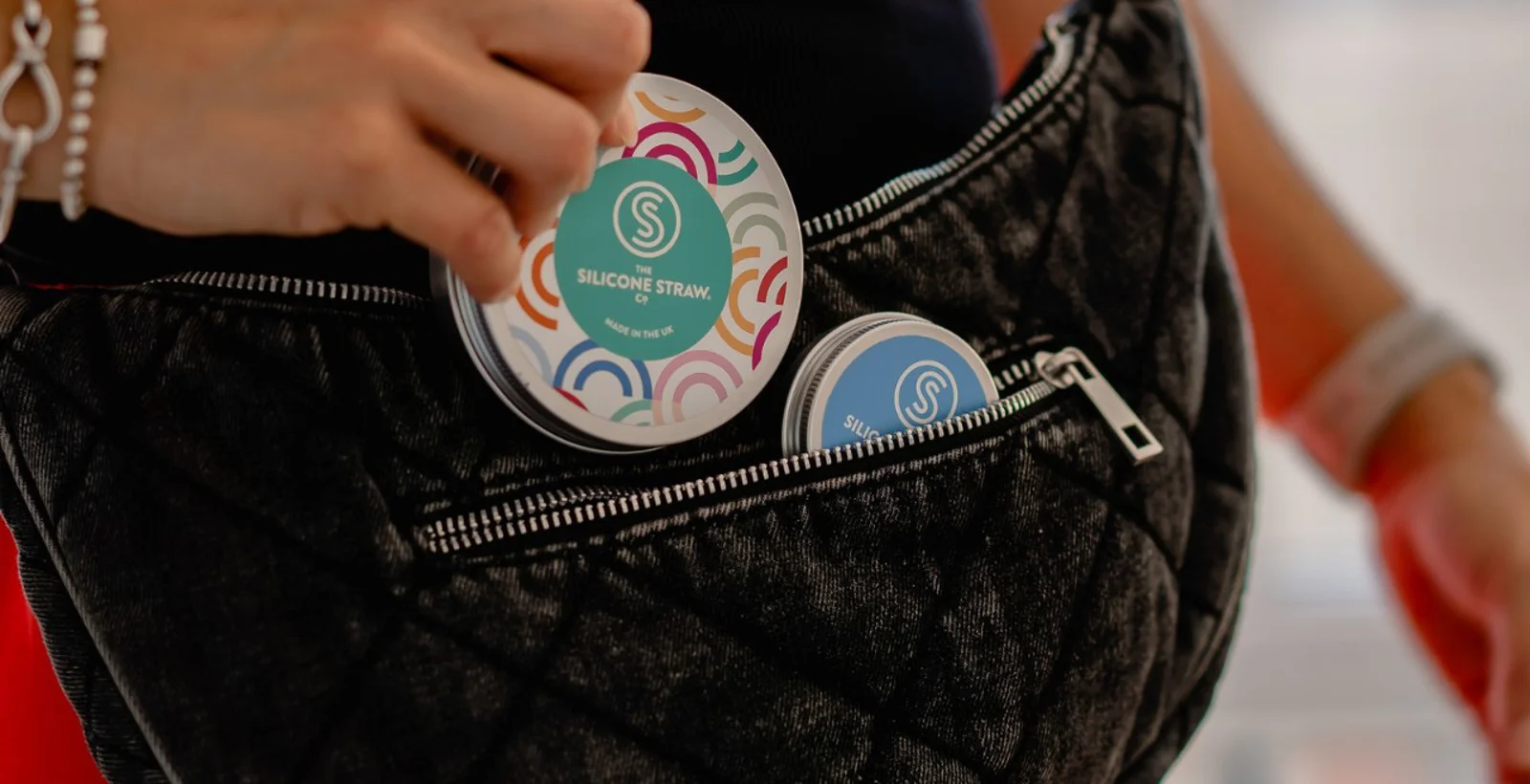 A silicone straw travel tin being tucked into a bag