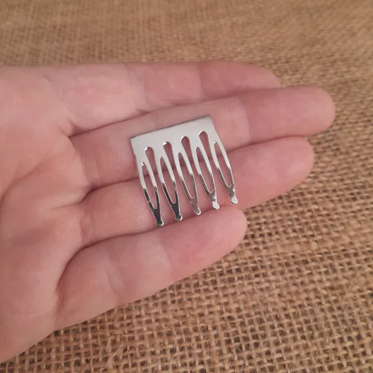 A miniature five prong silver metal doll comb blank, shown in a hand for scale, used for adult collector doll hair accessories and custom styling.