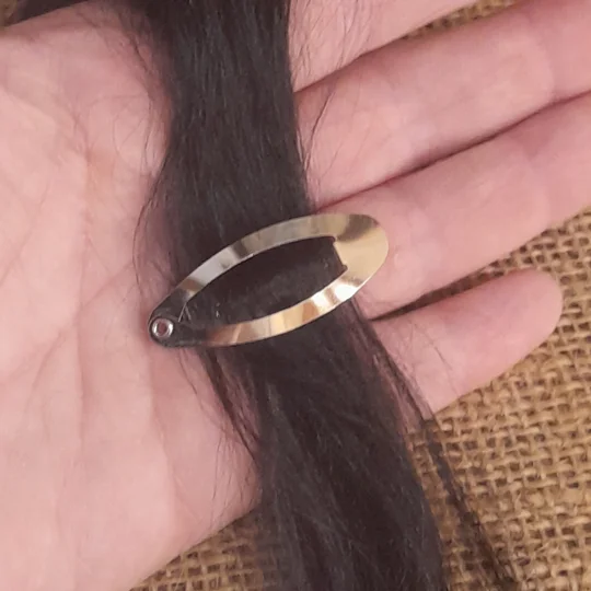 A miniature silver snap barrette fastened securely onto a lock of fine dark suri doll hair to demonstrate tension free styling for collector dolls