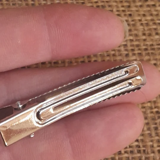Close up view of the underside of a miniature silver doll hair clip showing the smooth dual prong base configuration.