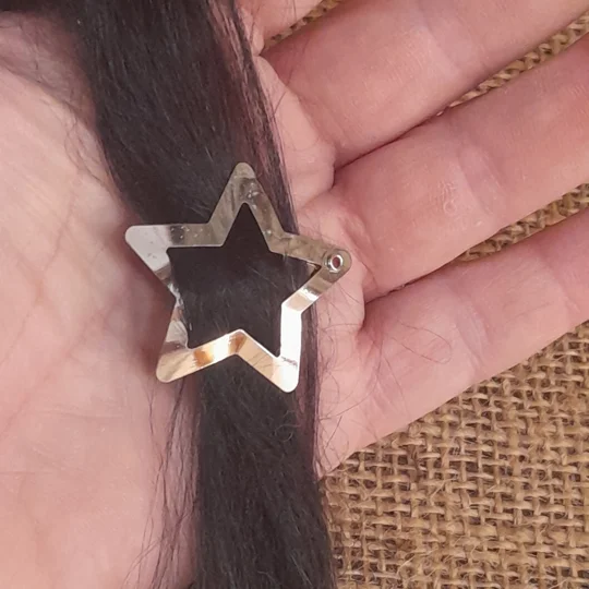 Close up view of a micro star shaped silver metal hair clip holding a strand of dark suri doll wig hair, ideal for adult collector doll customizing.