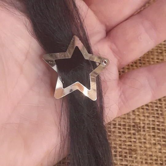 Close up view of a micro star shaped silver metal hair clip holding a strand of dark suri doll wig hair, ideal for adult collector doll customizing.