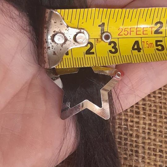 A silver metal star doll clip shown next to a yellow measuring tape to display its precise micro scale dimensions of roughly 3 centimeters.