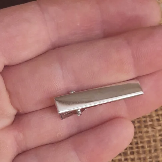 The top down perspective of a mini flat silver rectangular alligator clip blank held in a hand for scale
