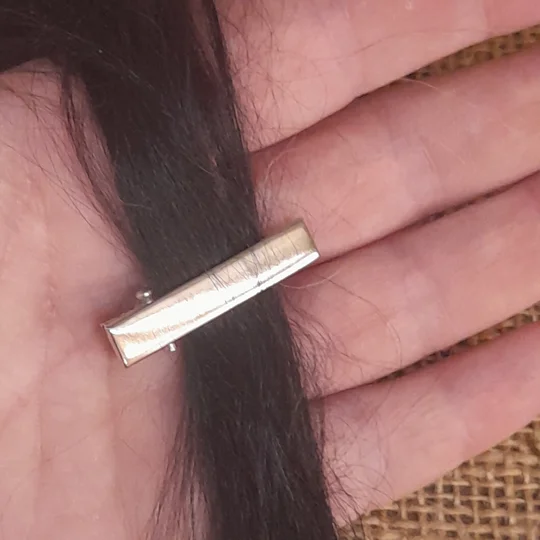 A micro silver alligator hair clip fastened onto a lock of fine dark suri doll hair to demonstrate secure placement.