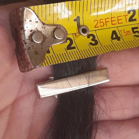 A silver metal doll clip shown directly beneath a yellow measuring tape to display its micro scale size of approximately 3 centimeters.