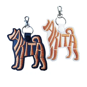 Black and white Akita dog word art keyrings made from faux leather with copper embroidered lettering and sturdy metal keyring fittings.