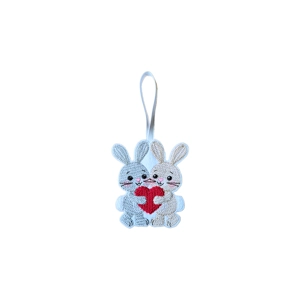 A felt bunny hanging decoration showing two bunnies holding a heart together, finished with knit-stitch style embroidery and a white hanging loop.