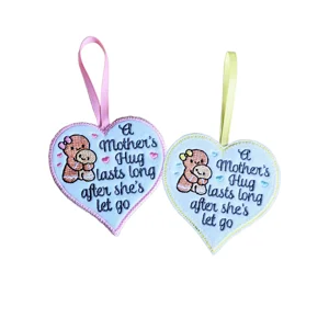 Two embroidered felt heart decorations with hanging ribbons, featuring a mum hugging her child and the wording 'A Mother's Hug Lasts Long After She's Let Go'.