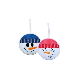 Two round felt snowman face ornaments, one Snowboy and one Snowgirl, each with a smiling stitched expression and a cosy winter hat, hanging from white ribbon loops.