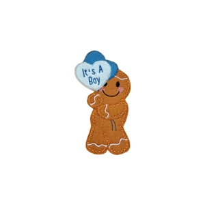 A felt gingerbread character with embroidered details, smiling face, and rosy cheeks, holding two heart-shaped balloons, the front balloon embroidered with ‘It’s a Boy’.