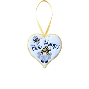 White felt heart hanging decoration embroidered with the words 'Bee Happy', a flying bee and a winged bee-themed gnome, finished with golden yellow edging and ribbon loop.
