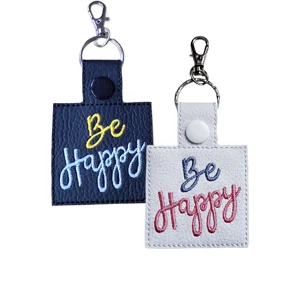 Be Happy embroidered faux leather keyrings and bag charms in black and white, with colourful stitched lettering and metal keyring clips.