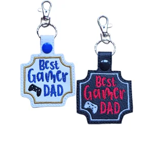Two Best Gamer Dad keyrings shown in black and white faux leather with embroidered lettering, controller detail and metal lobster clasps.