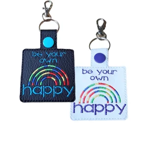 Be Your Own Happy embroidered faux leather keyrings in black and white, with colourful rainbow stitching and metal clips.