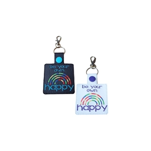 Two faux leather ‘Be Your Own Happy’ rainbow keyrings shown side by side. One is black and one white, each featuring embroidered text and a stitched rainbow design, with a rectangular shape and a metal keyring with lobster clasp.