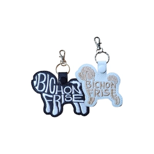 Two faux leather Bichon Frise-shaped keyrings, one black and one white, each featuring embroidered word-art spelling 'Bichon Frise' with metal keyring and clasp.
