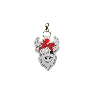 A faux leather highland cow keyring with stitched fringe, curved horns, and a large red bow-style bandana on its head, attached to a metal keyring and clasp.