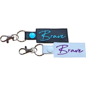 Black and white faux leather Brave positive word keyrings with embroidered text and metal clip attachments.